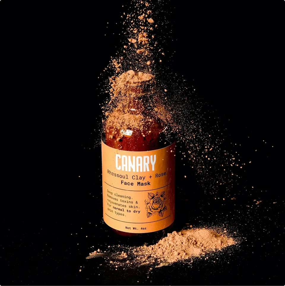 Canary Ghassoul Clay and Rose face mask jar surrounded by powder