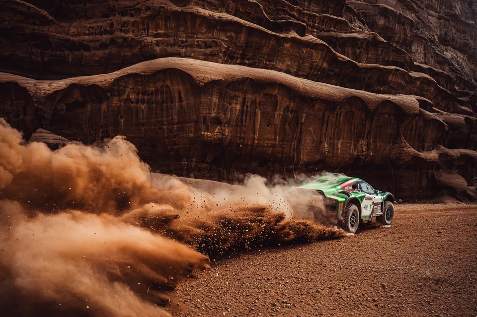 Off-road racing car throwing dust beneath a sandstone cliff